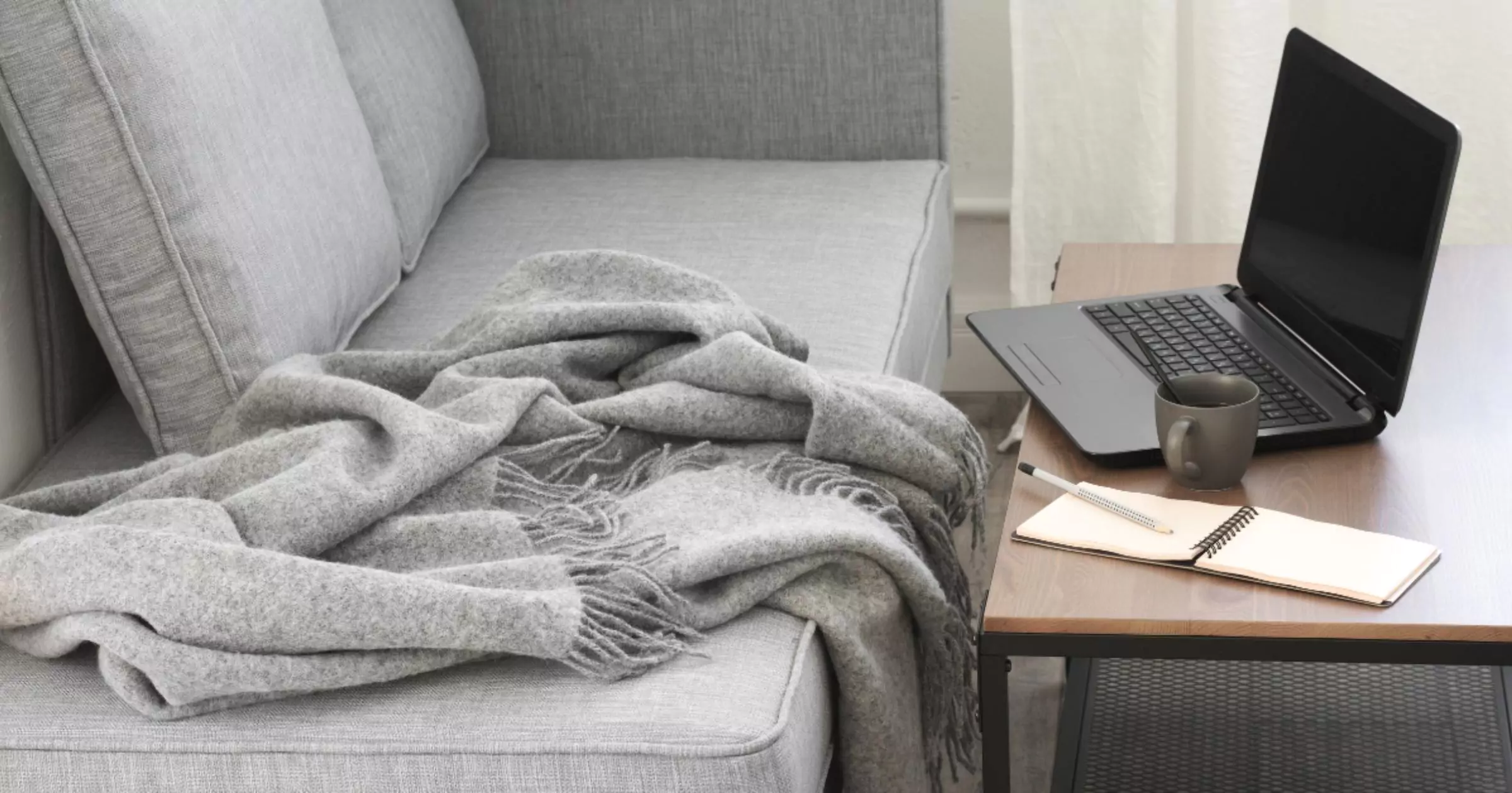laptop, notepad and mug on a table near grey sofa image